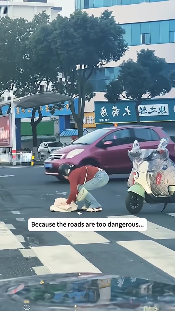 A person is kneeling down, wrapping a kitten in their coat on the side of the road.