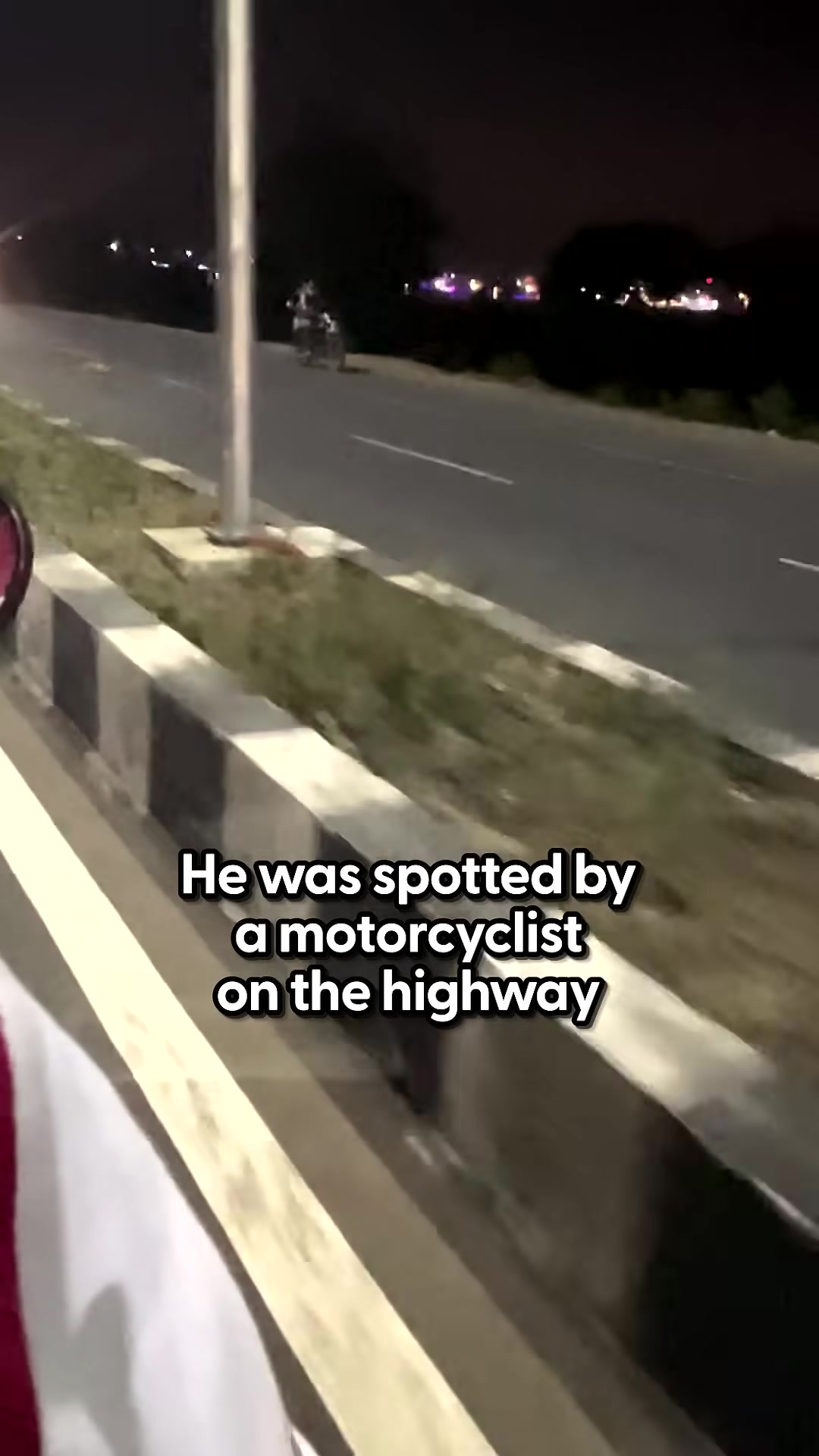 A motorcyclist stops near a dog lying on the highway at night.