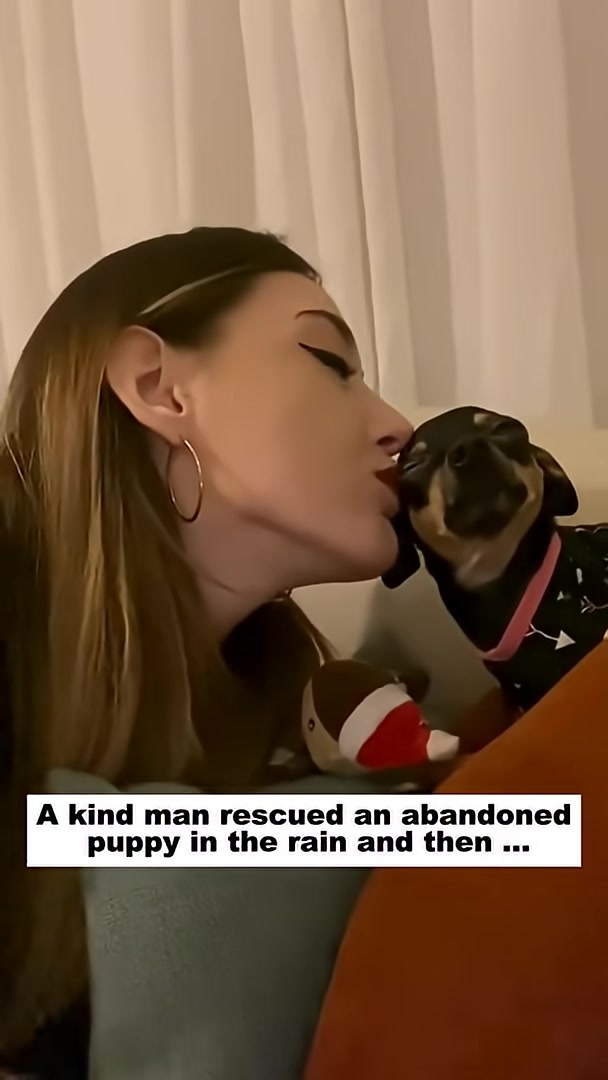 A woman gently kisses a small black puppy on the nose.