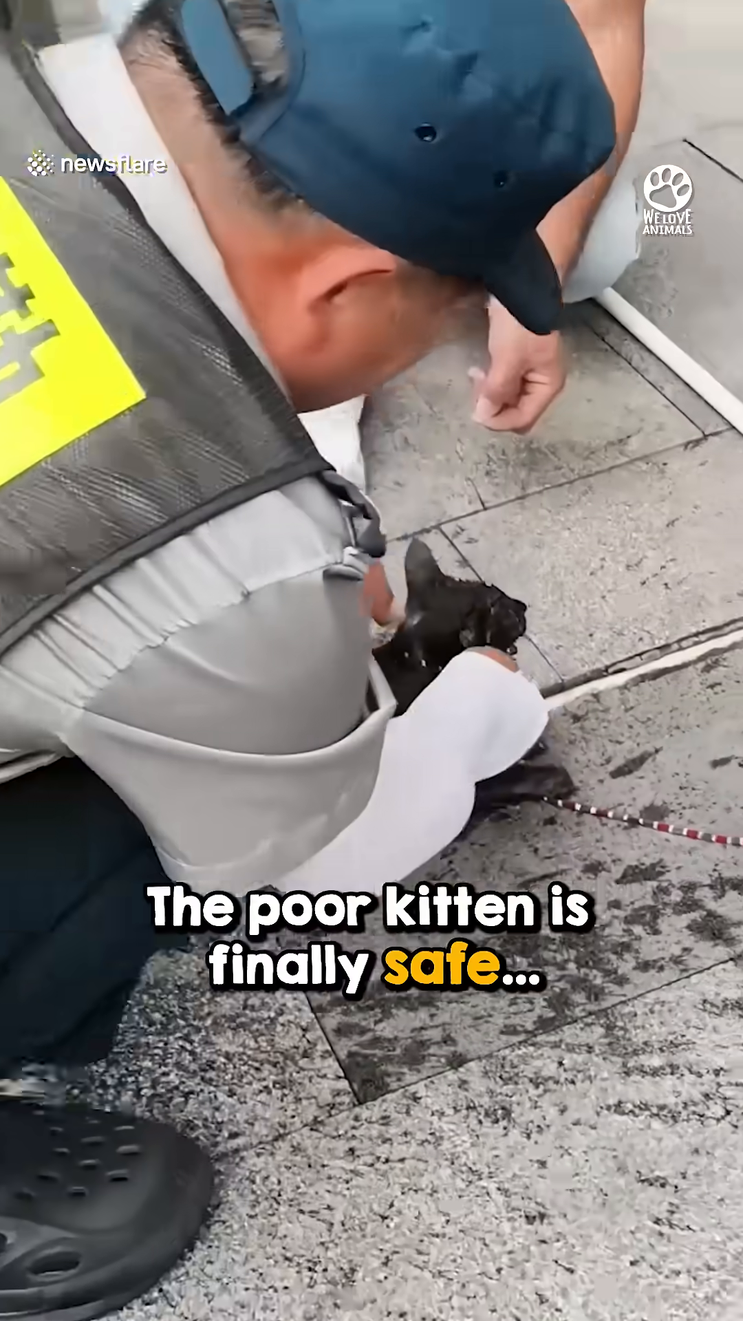 A wet and shivering black kitten lies on the ground, being attended to by rescuers.