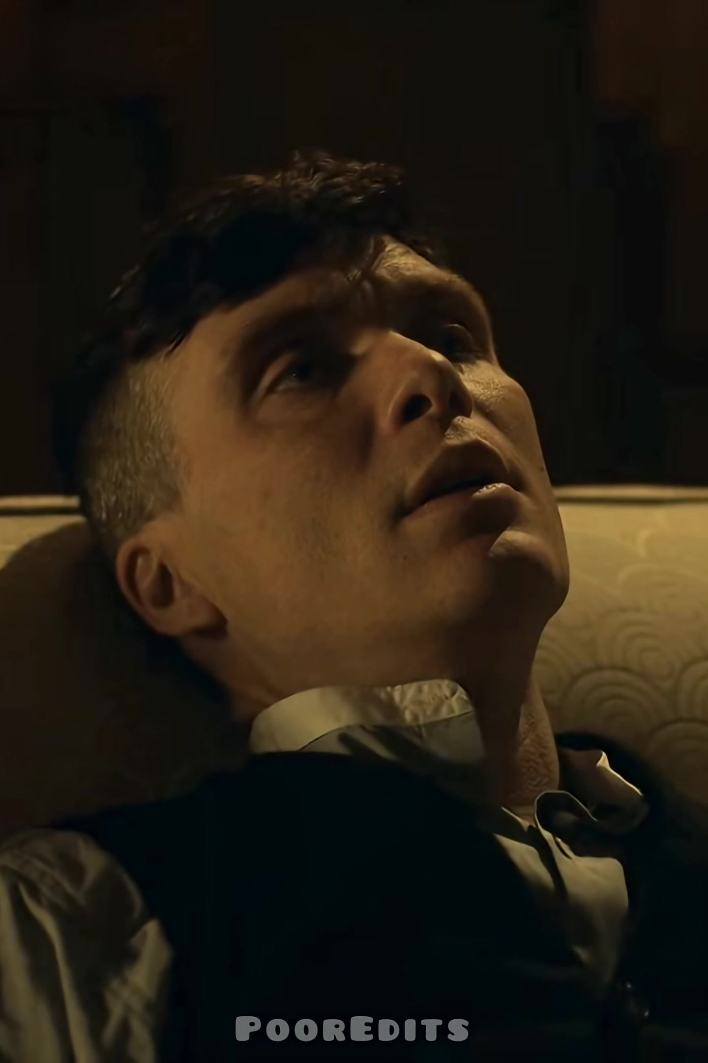 A man looks up with a pensive and serious expression in a dimly lit room.
