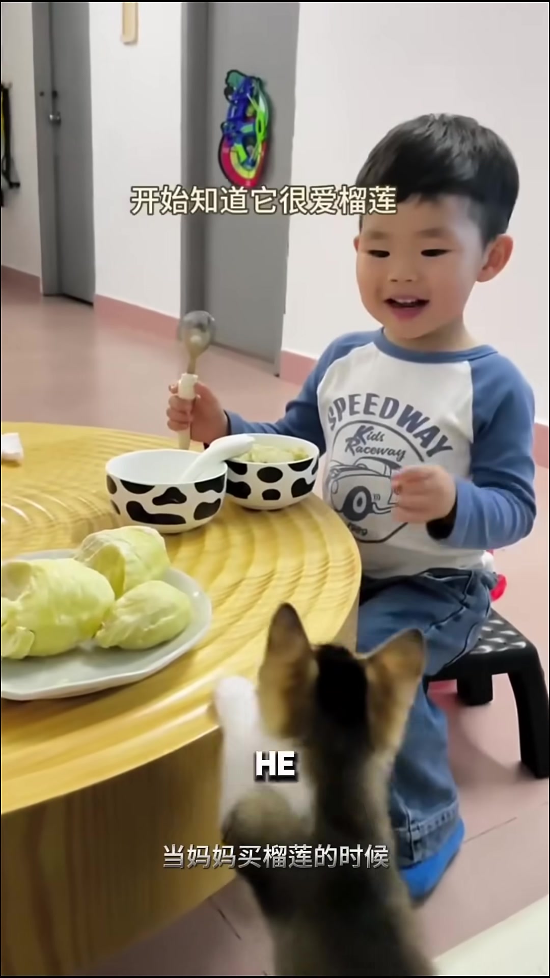 A little boy draws at a table while his kitten sits beside him, watching.
