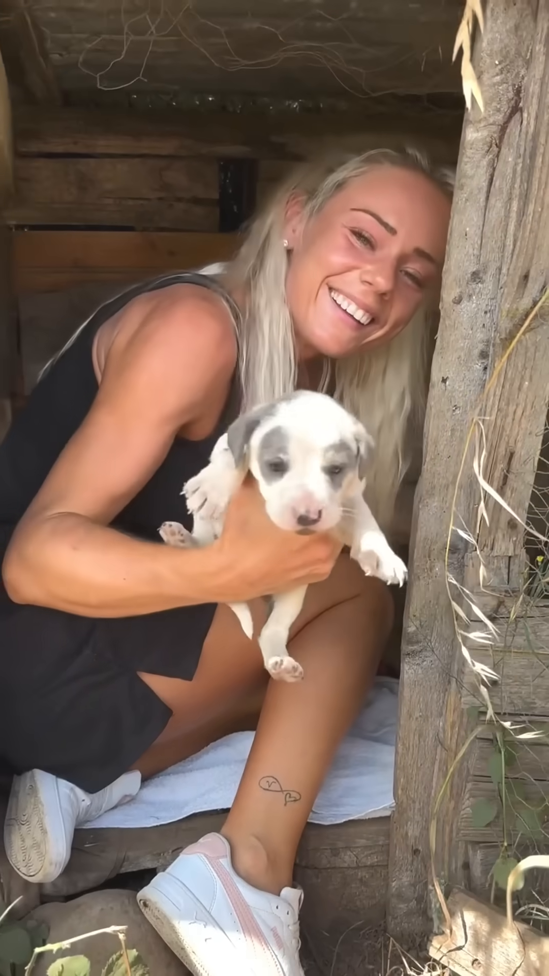 A woman gently holds a small, spotted puppy in a makeshift shelter.