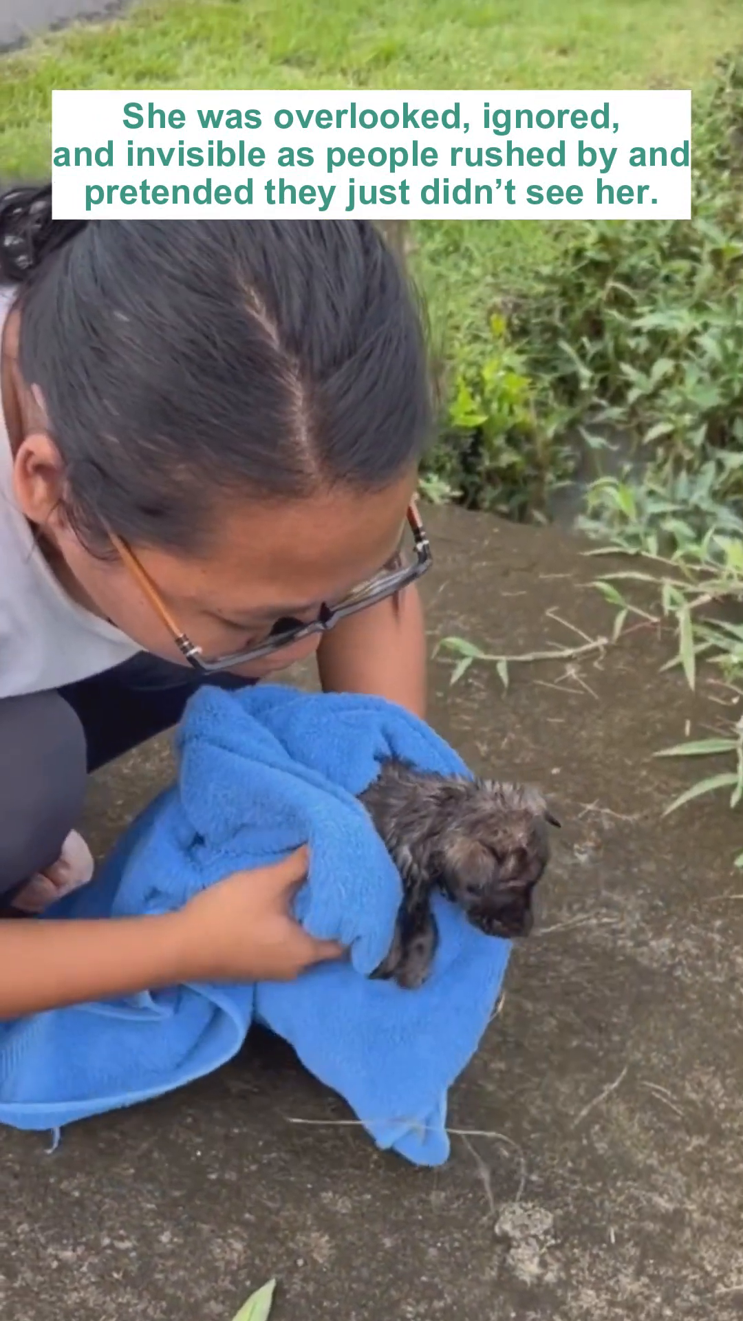 A person gently cradles a puppy wrapped in a blue towel, looking down at it with concern.