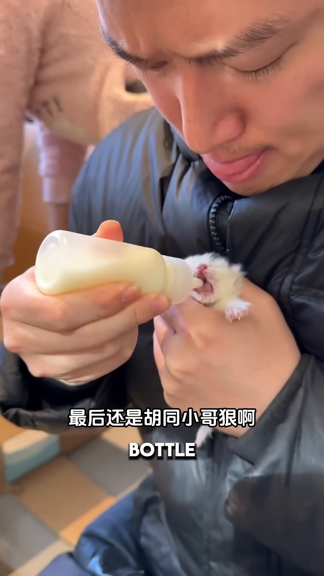 A person is carefully bottle-feeding a tiny newborn kitten with milk.