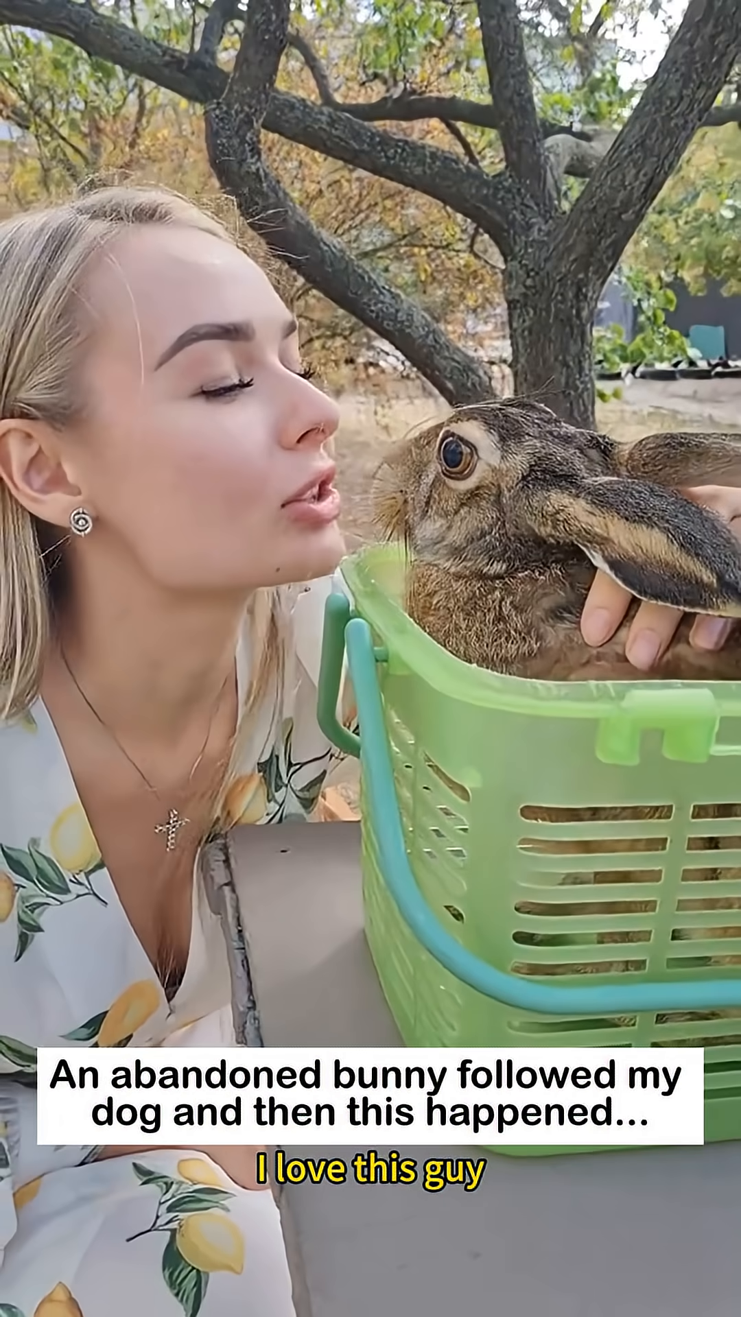 A woman gently kisses a bunny that is sitting in a green basket.